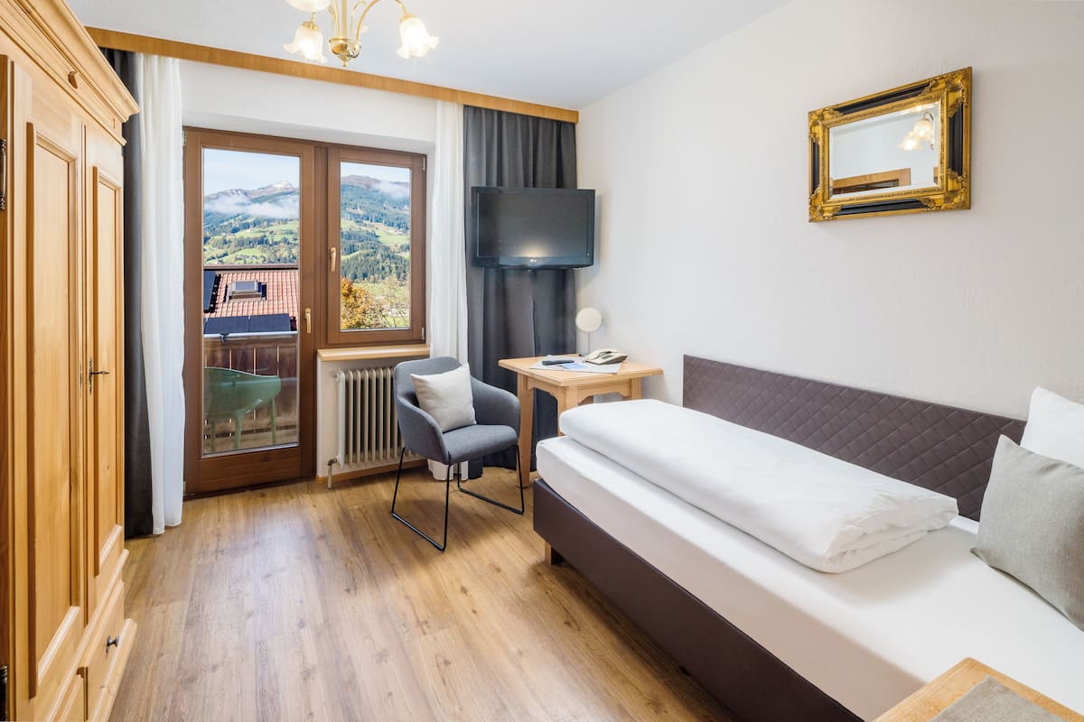 A hotel room with a bed, a desk, a chair, a TV, and a view of the outdoors.