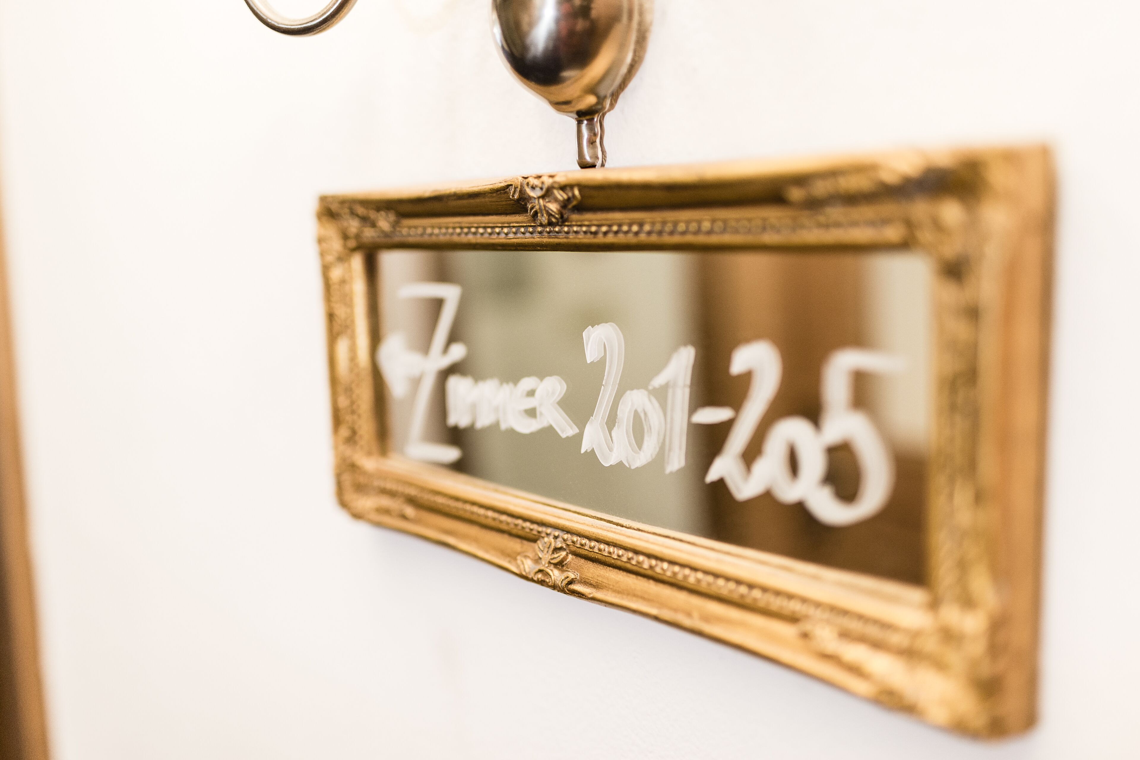 A gold-framed mirror with the inscription "Zimmer 201-205" on a white wall.