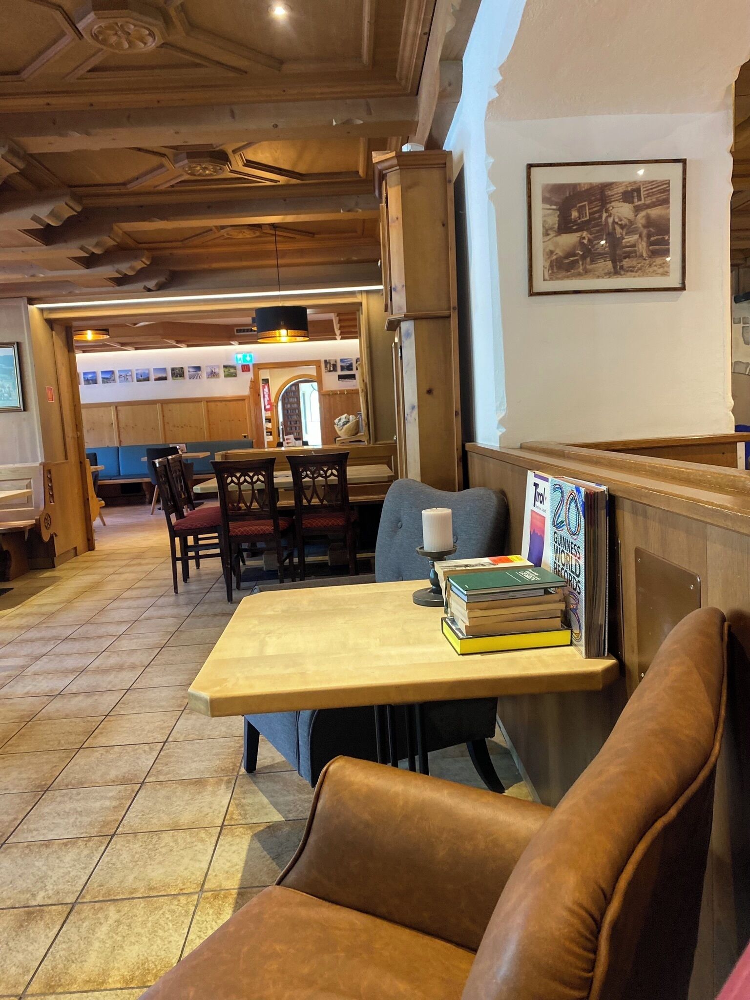 A cozy restaurant interior with wooden furniture, a table with books, and a framed picture on the wall.