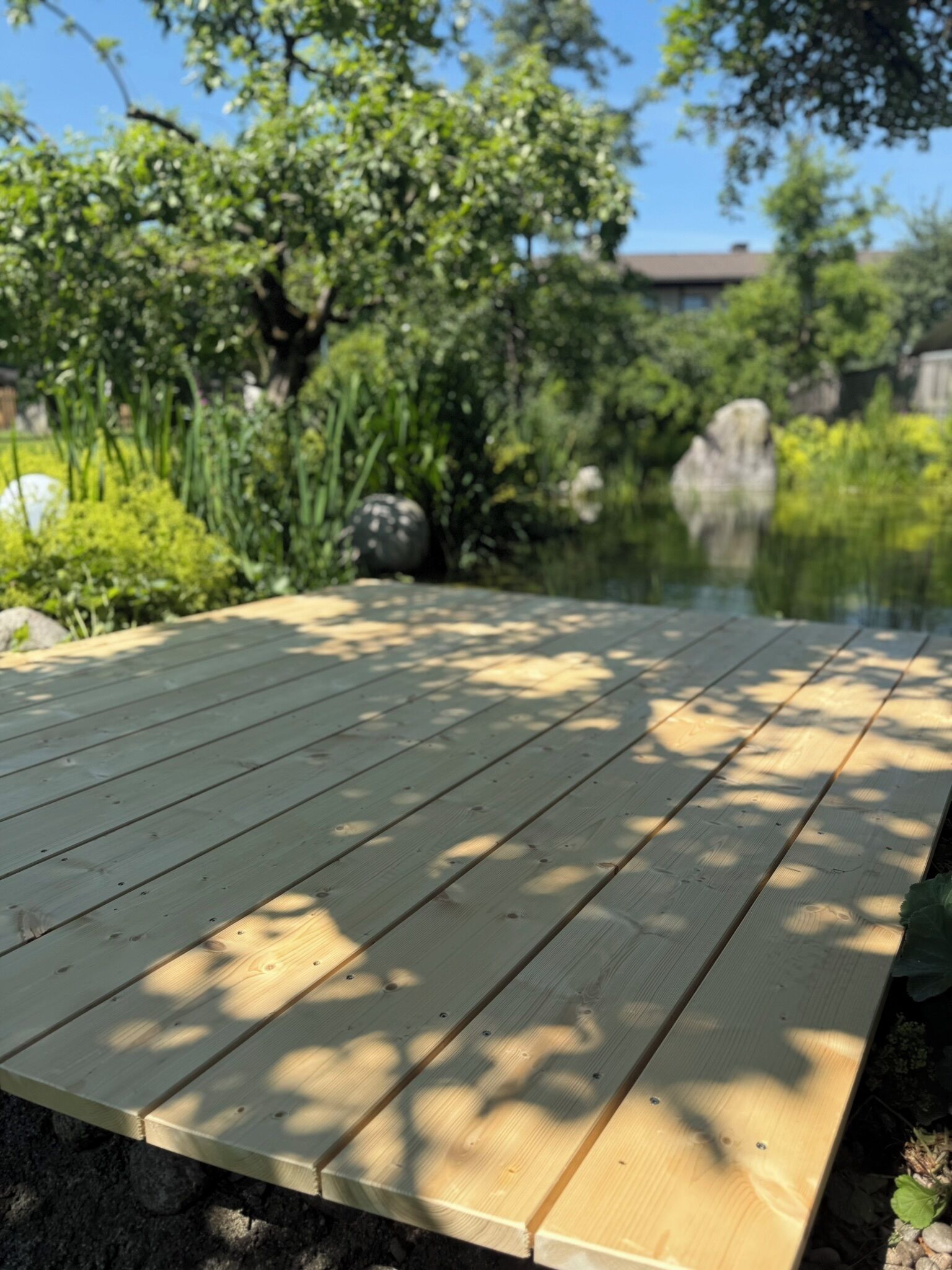 Eine Holzterrasse mit Teich und Grünflächen im Hintergrund.