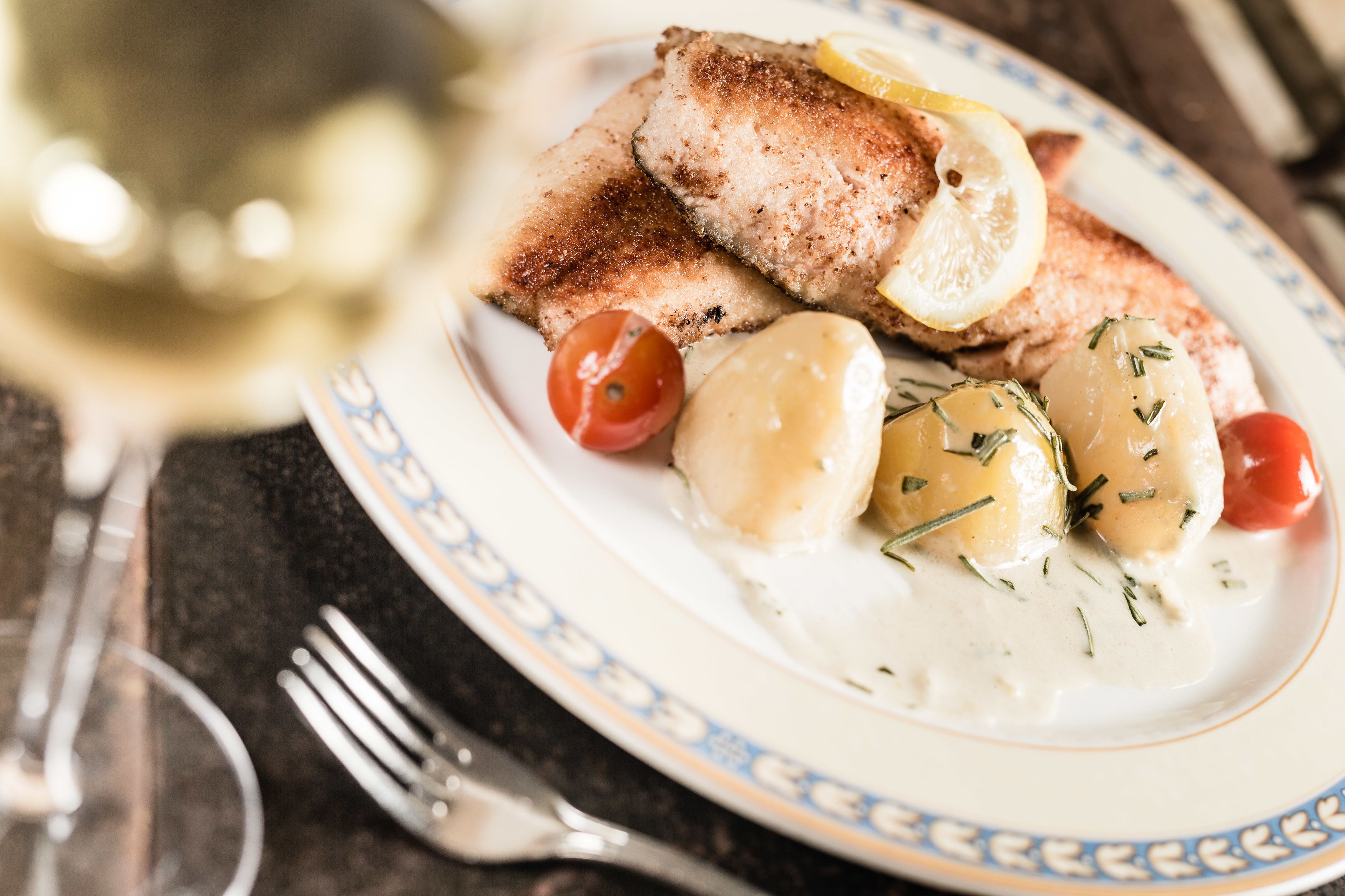 Ein Teller mit gegrilltem Fisch, Zitronenscheiben, Cocktailtomaten und gekochten Kartoffeln.