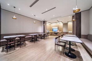 A modern dining area with multiple tables and benches, a kitchen in the background, and pendant lighting.