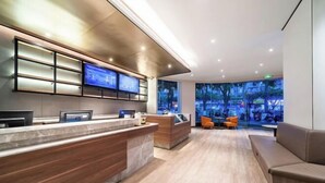 A modern reception area with a marble counter, wooden reception desk, and multiple monitors. There are seating areas with orange chairs and a sofa. - HanTing Hotel (Chongqing Jiazhou Huahuiyuan Subway Station) (Chongqing)