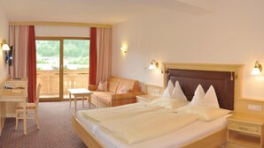 Ein Hotelzimmer mit einem großen Bett, einem Schreibtisch, einem Stuhl, einer Couch und einem Balkon mit Vorhängen.