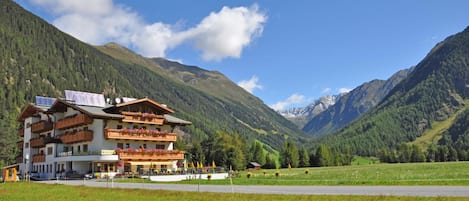 A multi-story hotel with balconies, a ski resort in the background, and a clear sky.
