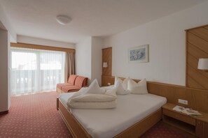 A hotel room with a bed, a chair, a bedside table, and a window with curtains.