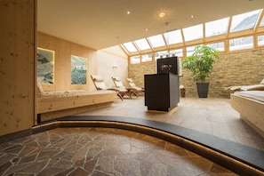 Un área de spa con suelo de madera, pared de piedra, una camilla de masaje negra y un ventanal grande.