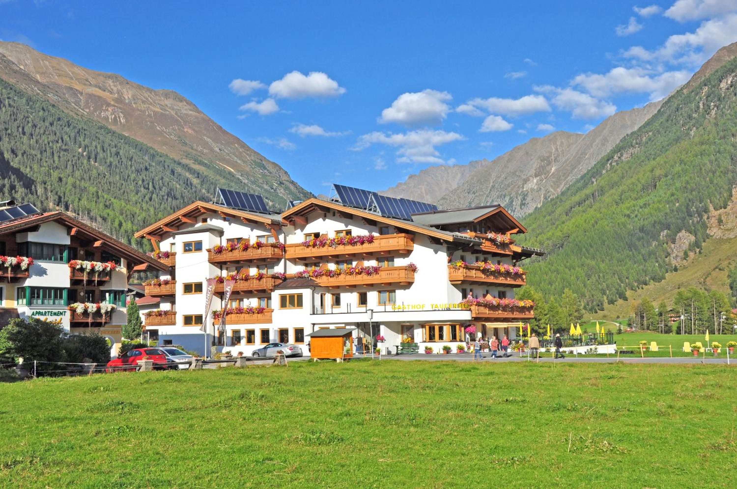 Un hotel de varios pisos con balcones decorados con flores, paneles solares en el techo y un telón de fondo montañoso.
