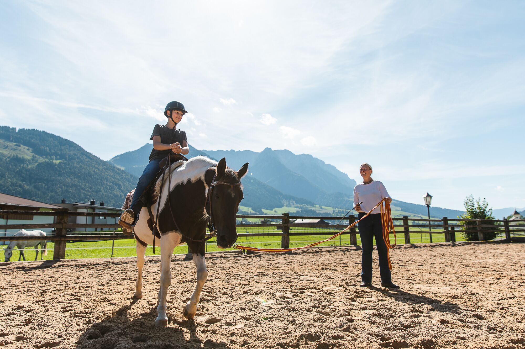 A person riding a horse in an outdoor arena with mountains in the background.