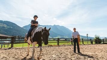 A person riding a horse in an outdoor arena with mountains in the background.