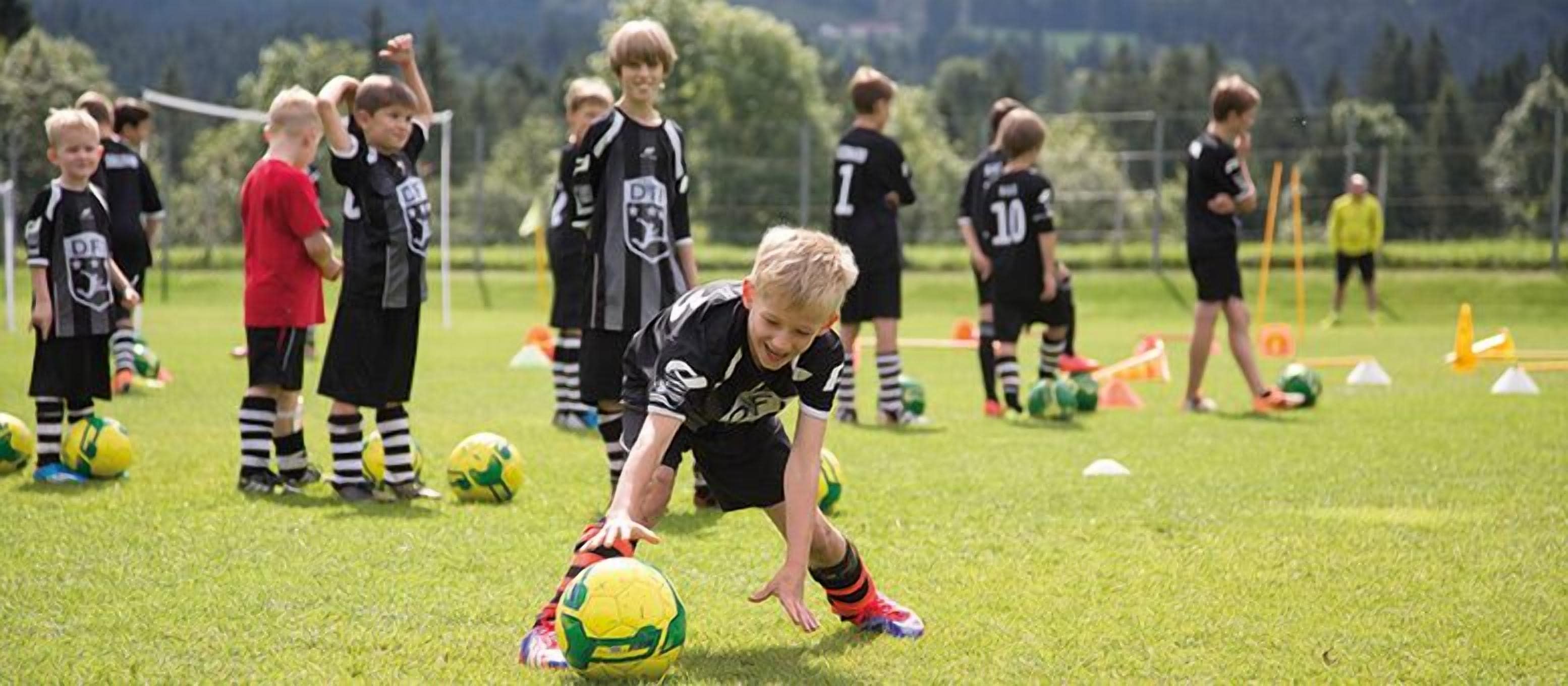 A group of children playing soccer on a grassy field with training equipment.