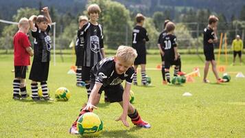 En grupp barn som spelar fotboll på en gräsplan med träningsutrustning.