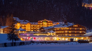 A large, multi-story hotel with a snow-covered roof, illuminated windows, and a prominent sign. - Hotel Seehof (Koessen)