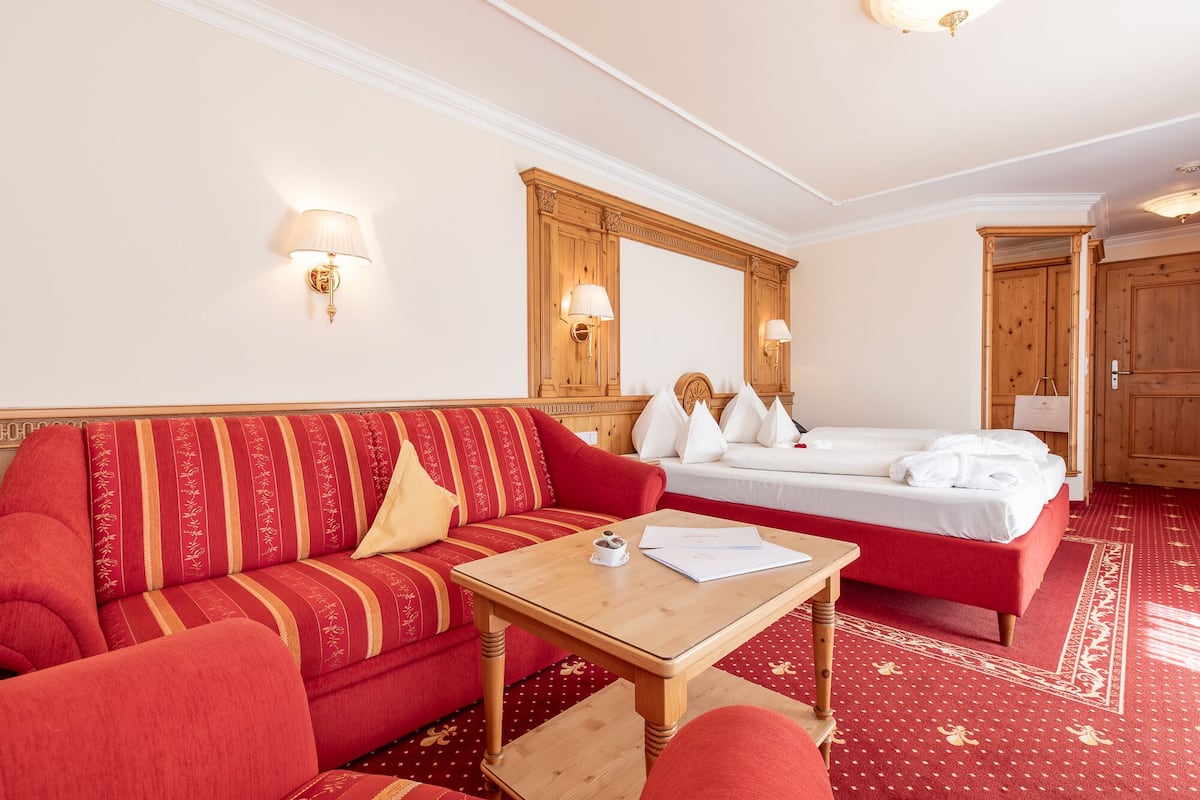Una habitación de hotel con un sofá rojo, una mesa de madera, una cama con ropa blanca y un armario de madera.
