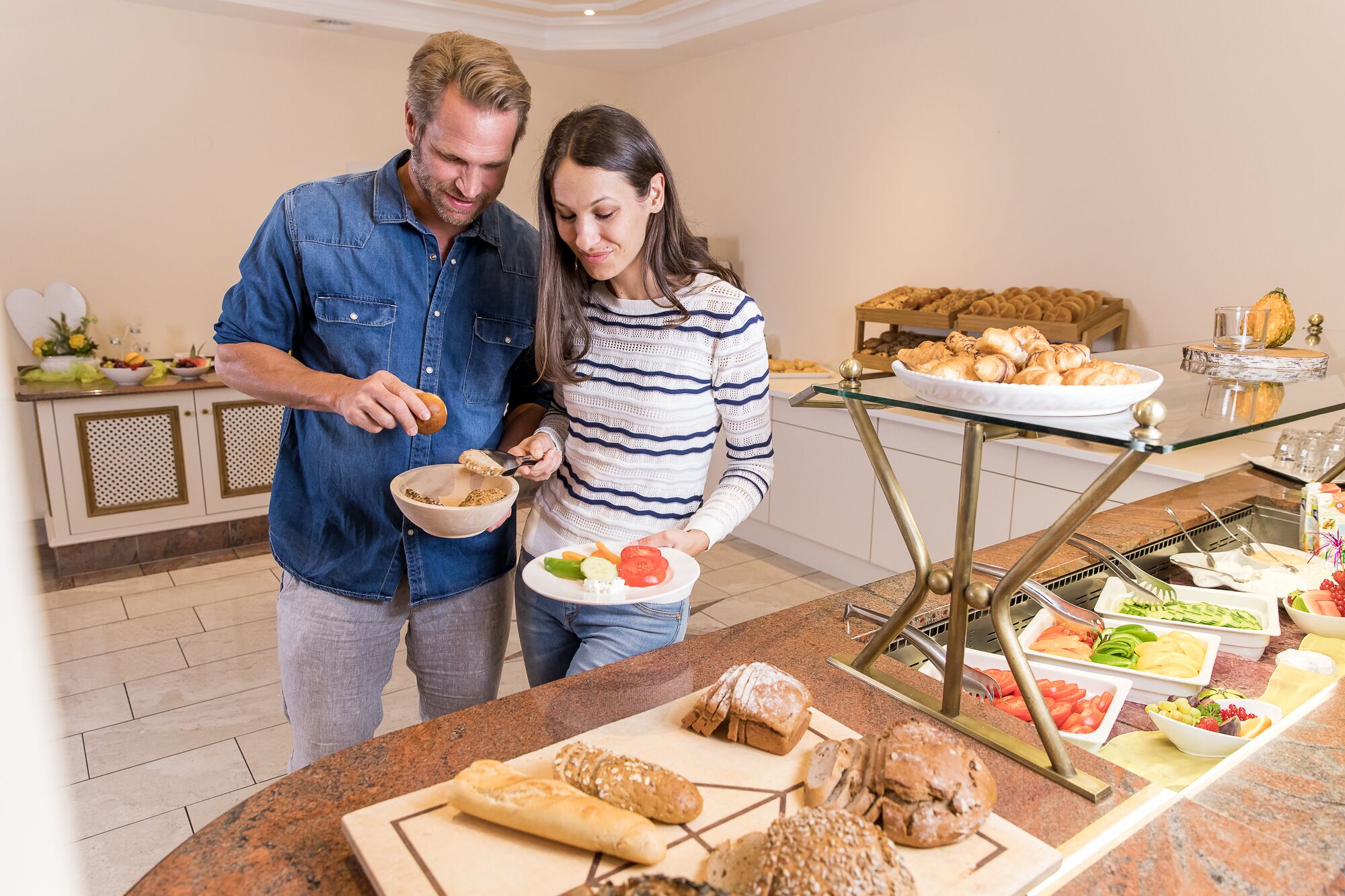 A buffet setup with various food items and a man and woman preparing food.