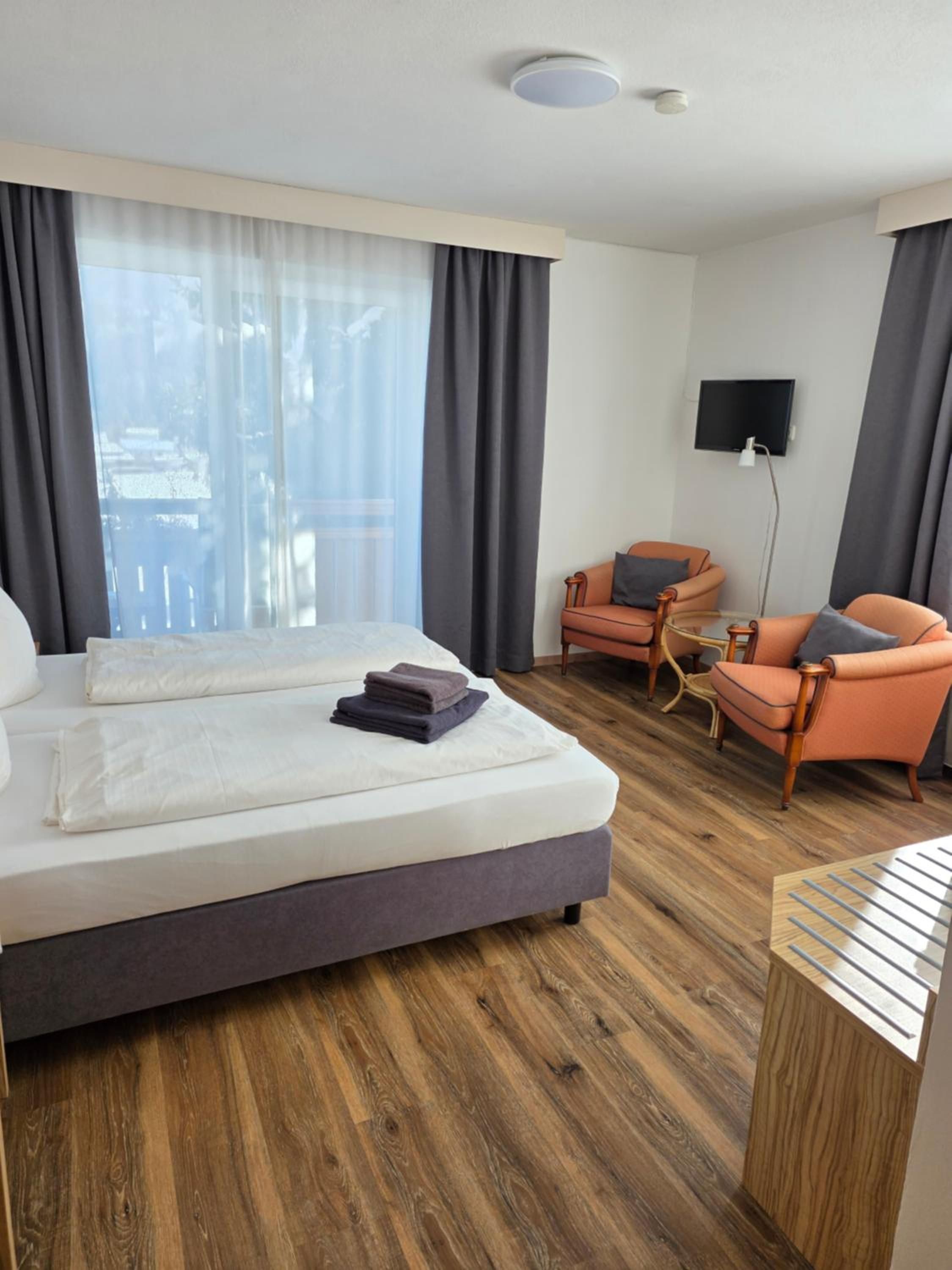 A hotel room with a bed, two armchairs, a TV, and a window with curtains.