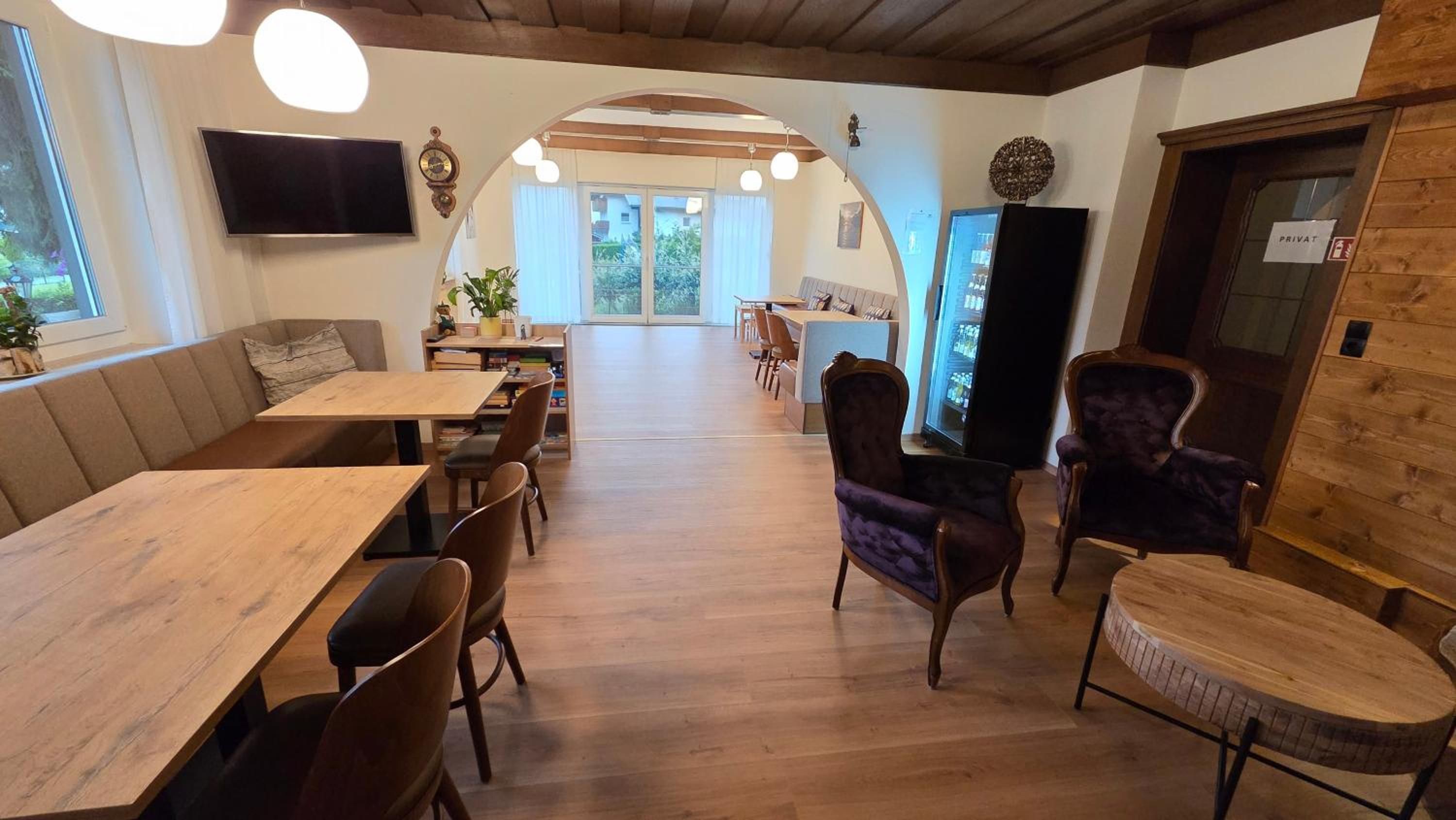 A spacious room with a wooden floor, a sofa, a dining table, and chairs. There is a television mounted on the wall, and a door labeled 'PRIVATE' with a fire alarm sticker.