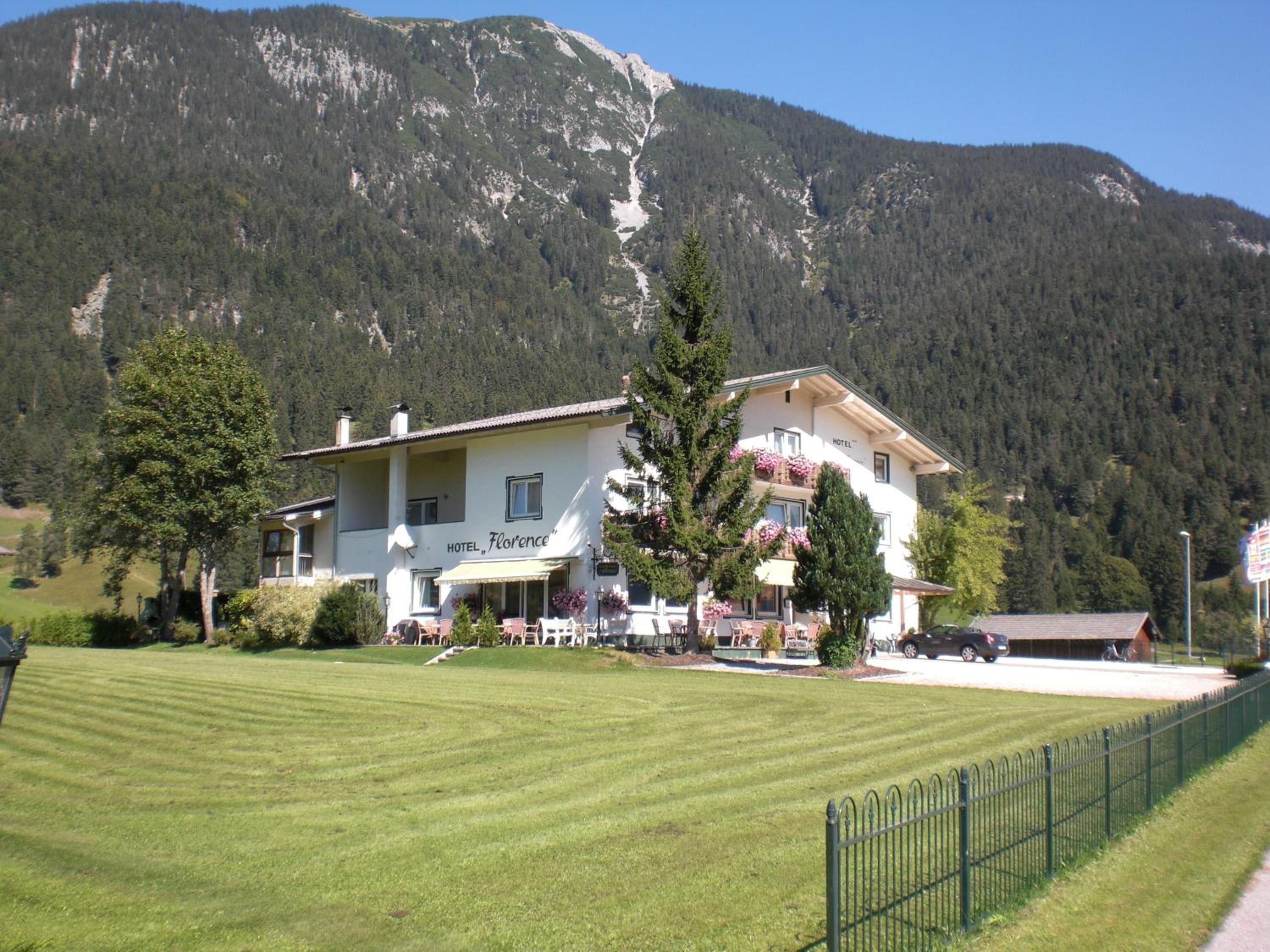 Un hotel con balcón, césped y montañas al fondo.