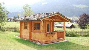 A wooden cabin with a porch, surrounded by a wooden fence and a grassy field. - Pension Sonnblick (WESTENDORF)