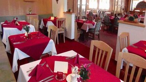Un restaurant avec de nombreuses tables, recouvertes de nappes rouges, agrémentées de couverts blancs et de chaises en bois.