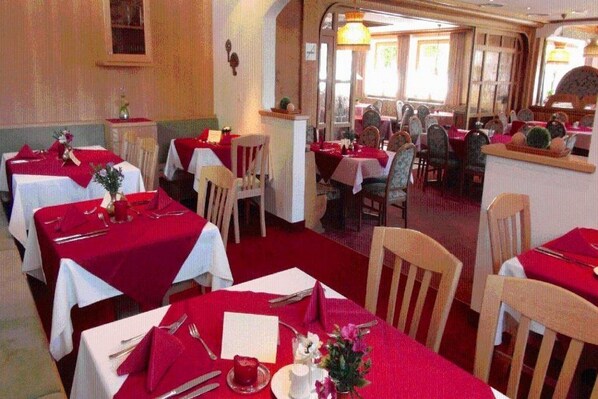 Un restaurant avec de nombreuses tables, recouvertes de nappes rouges, agrémentées de couverts blancs et de chaises en bois.