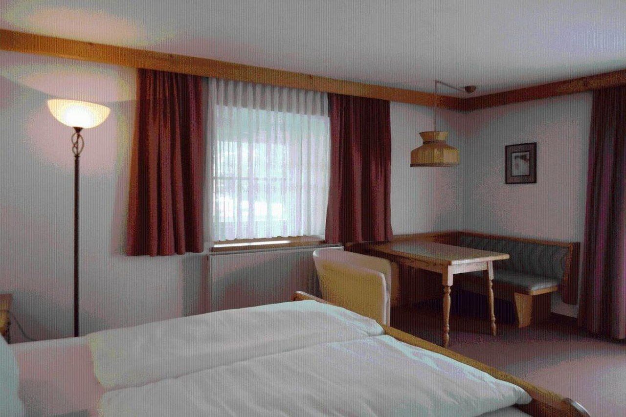 Habitación de hotel con cama, escritorio, silla, lámpara y ventana con cortinas.