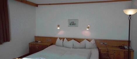 A hotel room with a single bed, wooden headboard, bedside tables, a nightstand, a lamp, and a framed picture on the wall.