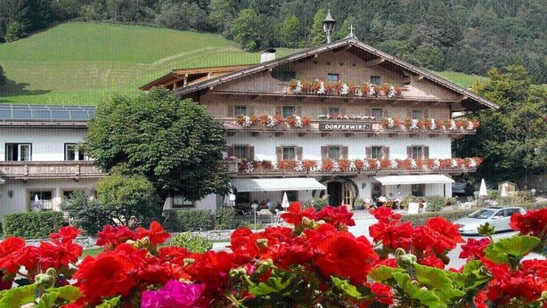 Un bâtiment de style chalet traditionnel, sur lequel on peut lire l’inscription « Dorfperwirt ».