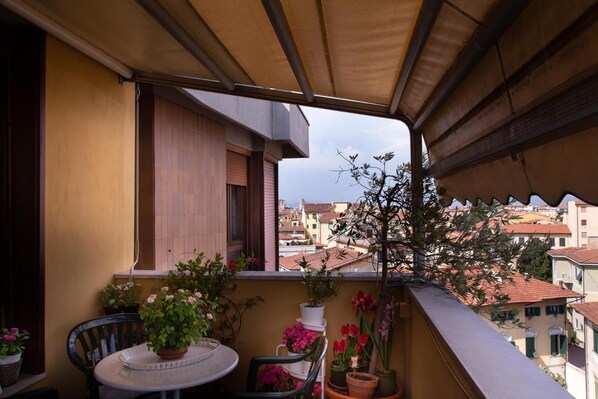 A balcony with a table and chairs, potted plants, and a view of buildings in the distance.