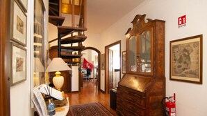 A hallway with a wooden staircase, a large wooden cabinet, and a fire extinguisher on the wall.