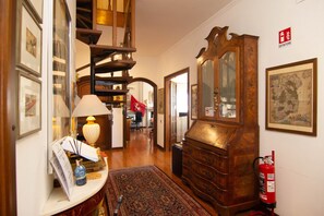 A hallway with a wooden staircase, a large wooden cabinet, and a fire extinguisher on the wall.