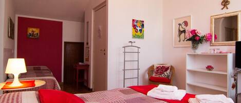 A hotel room with a bed, a desk, a chair, a mirror, and a shelf with towels.