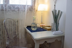A bathroom with a shower chair, a glass bottle, a small table with a lamp, and a vase with reeds.