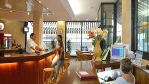 Uma área de recepção de hotel com um balcão de madeira, um monitor de computador e um vaso com flores.