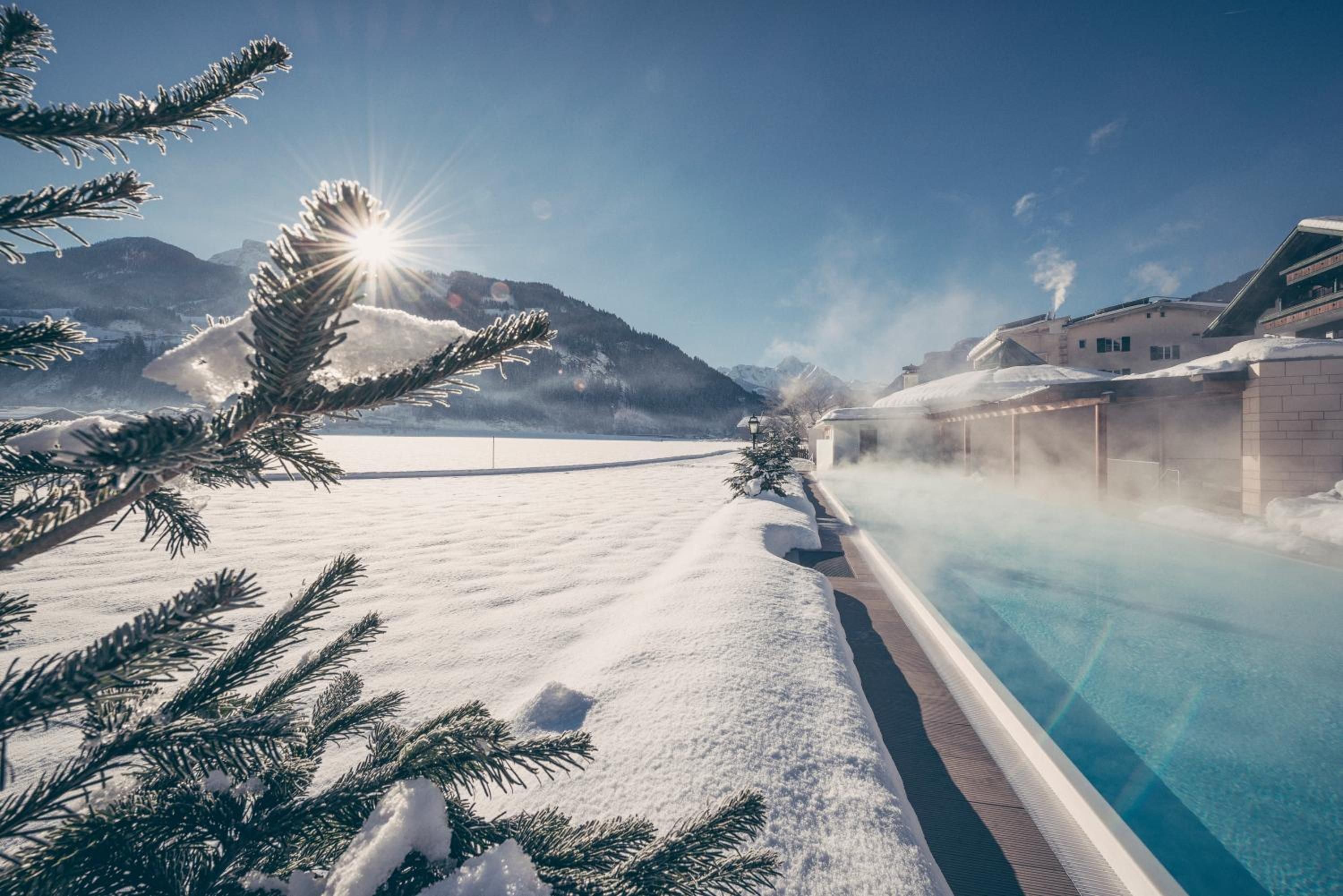 Un paysage enneigé avec une piscine, des montagnes en arrière-plan et un bâtiment dont la vapeur s'échappe du toit.