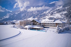 En snötäckt bergsanläggning med en stor byggnad som har flera balkonger och en swimmingpool.