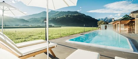 A pool area with lounge chairs and umbrellas, surrounded by a mountain landscape.