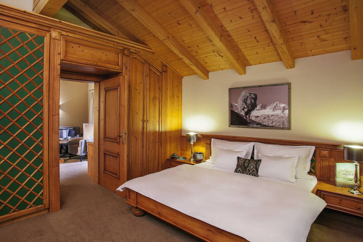 A wooden bedroom with a bed, a nightstand, a lamp, and a painting on the wall.