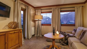 Quarto de hotel com um armário de madeira, uma mesa redonda com garrafa e copo, uma luminária e um sofá.