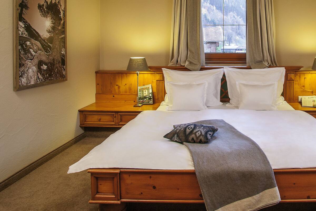 A large bed with white linens and a gray throw blanket, flanked by wooden nightstands with lamps and a framed picture.