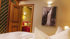 Quarto de hotel com uma cama, porta de madeira, quadro com uma cachoeira e uma cadeira vermelha ao fundo.