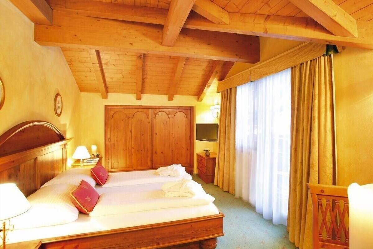 A hotel room with a wooden bed, a wooden wardrobe, a television, and curtains.