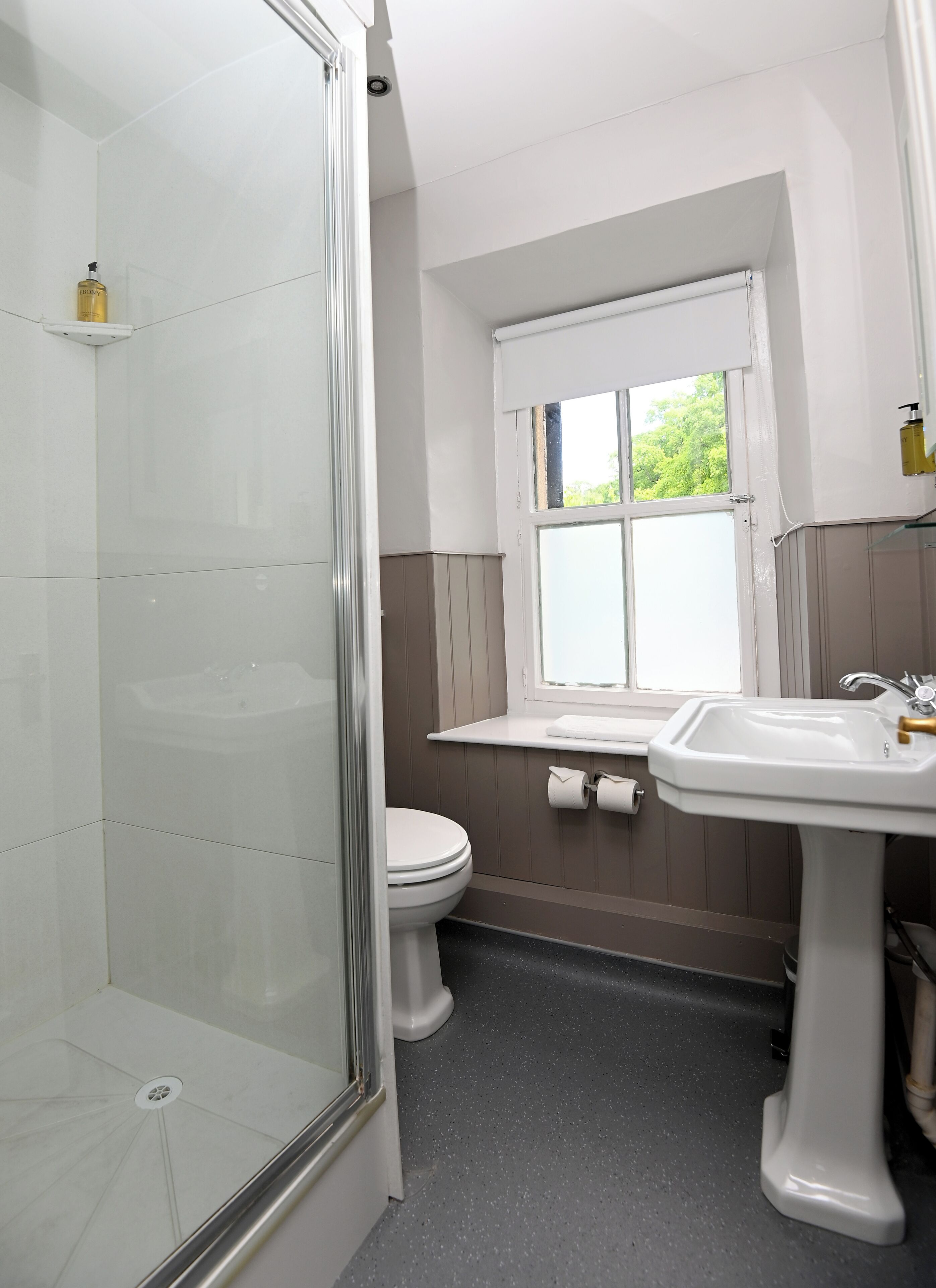 Un baño con cabina de ducha de vidrio, inodoro, lavamanos y ventana.
