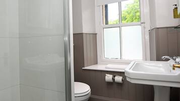 Un baño con cabina de ducha de vidrio, inodoro, lavamanos y ventana.