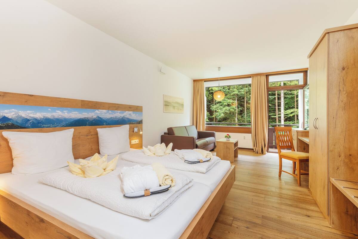 A bedroom with a large bed, wooden headboard, and a view of the outdoors through large windows.