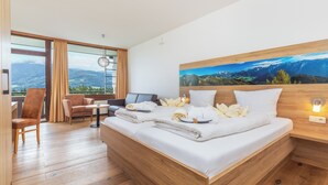 Habitación de hotel moderna con una cama grande, un escritorio, una silla y vistas a montañas a través de amplios ventanales.