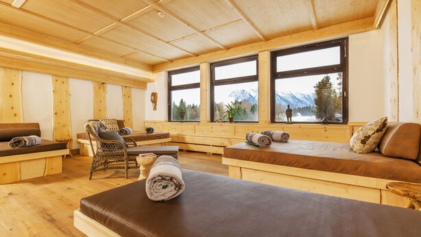 Interior de madera con ventanas amplias, un sofá, una silla y una mesa para masajes.