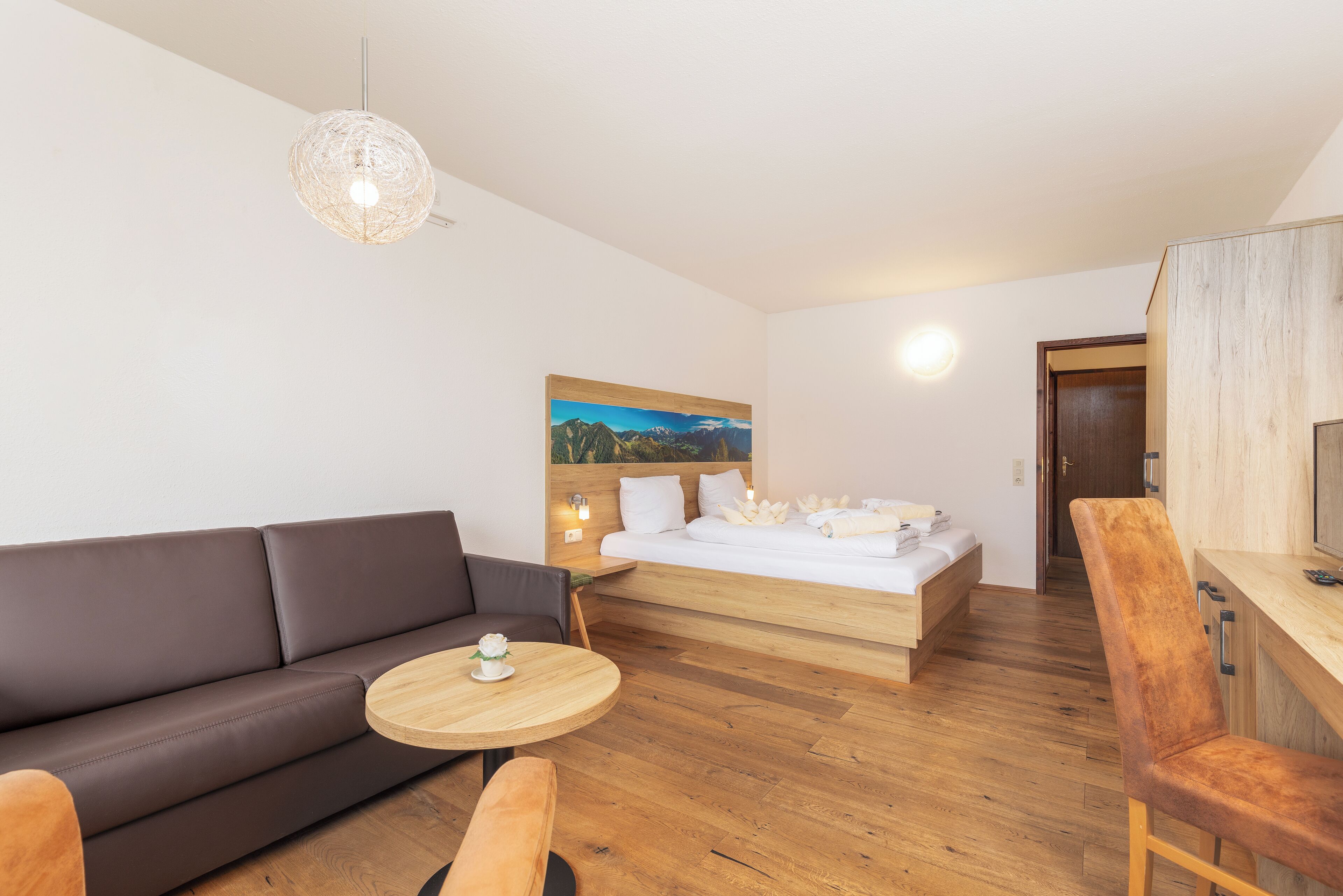 Un dormitorio moderno con una cama de madera, un sofá, una mesa redonda de madera y un cuadro en la pared.