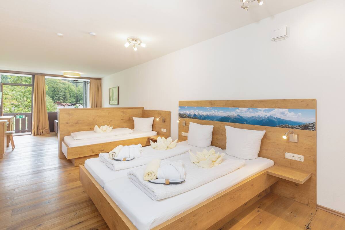 A hotel room with two beds, wooden headboards, white linens, and a painting of mountains.