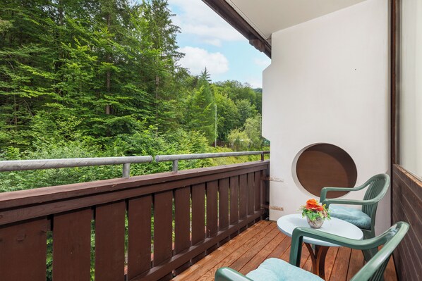 A balcony with a wooden railing, a round table with a flower vase, and green chairs. - Alpenhotel Dachstein (Bad Goisern)